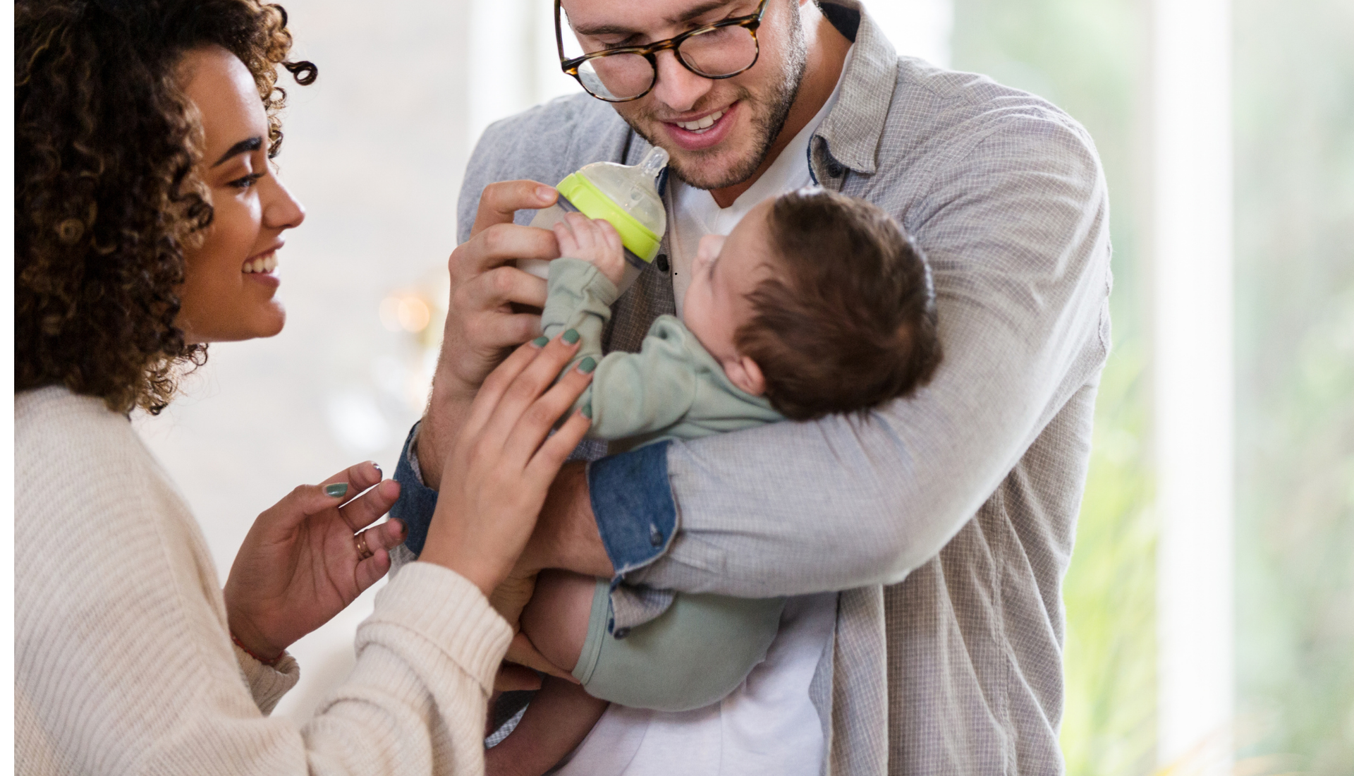 A mother and father hold and feed their newborn baby